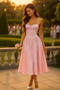 Elegant pink corset bodice dress for women, midi length, with spaghetti straps and a full skirt, shown with a woman in a garden setting on a wedding, holding a pink rose.